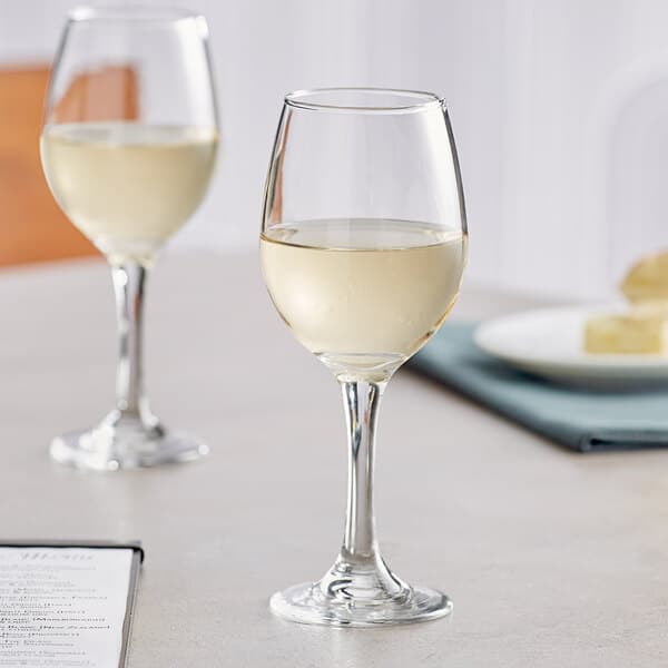 Two Acopa all-purpose wine glasses of white wine on a table.