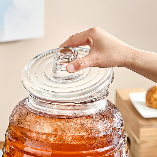 A hand holding a glass jar with an Acopa barrel beverage dispenser lid