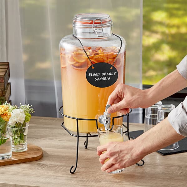 A hand pouring blood orange sangria from an Acopa glass beverage dispenser into a glass.