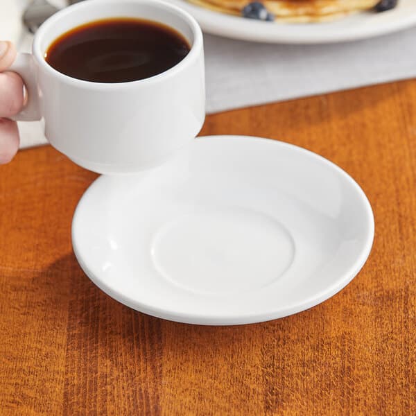 A hand holding a cup of coffee on a white Acopa stoneware saucer.