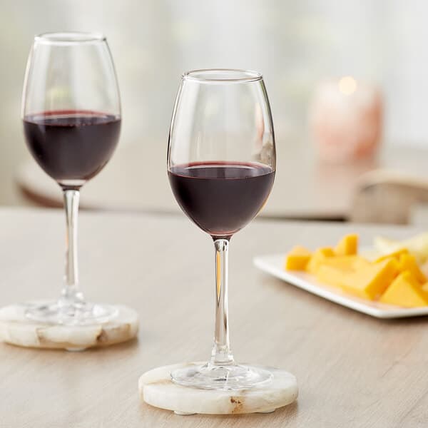 Two Acopa Select Blanc wine glasses on a table with wine and cheese.