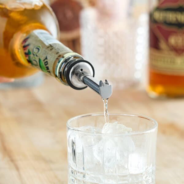 A stainless steel liquor pourer with a flip cap attached to a bottle, pouring liquid into a glass with ice.