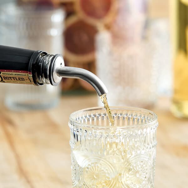An angled stainless steel liquor speed pourer dispensing liquid into a glass.