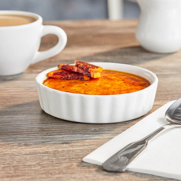 An Acopa white porcelain bowl filled with food on a table with a spoon.