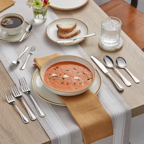 A table set with a bowl of soup, a spoon, and silverware.