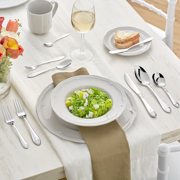 A white table with a bowl of food, a plate, and Acopa Monaca stainless steel spoons.