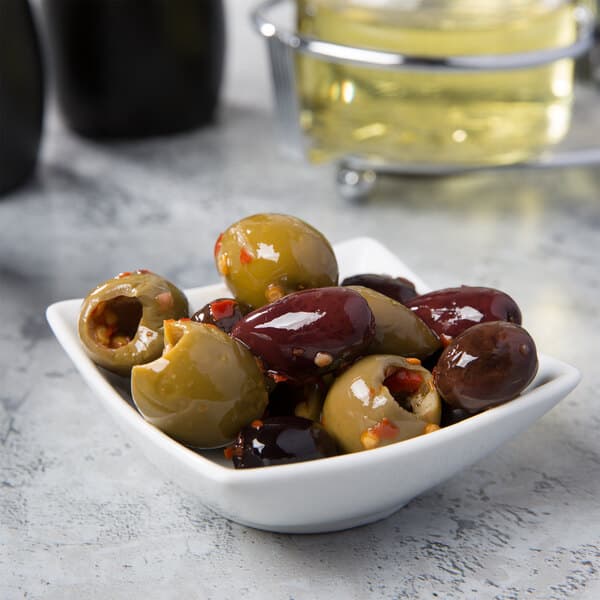 A white Acopa square sauce cup filled with green olives.