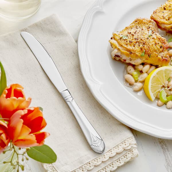 A plate of food with a knife and Acopa Monaca table knife next to a lemon wedge and beans.