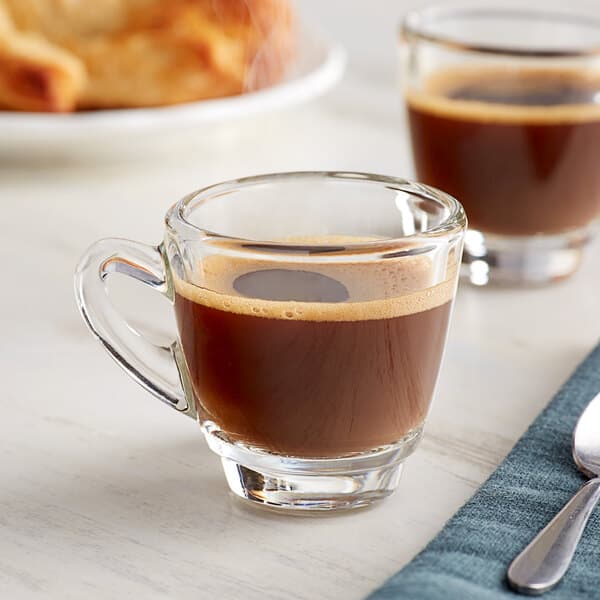 An Acopa espresso cup filled with coffee on a table with a spoon and fork.