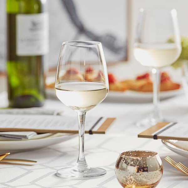 An Acopa Radiance white wine glass filled with white wine on a table with a gold plate.