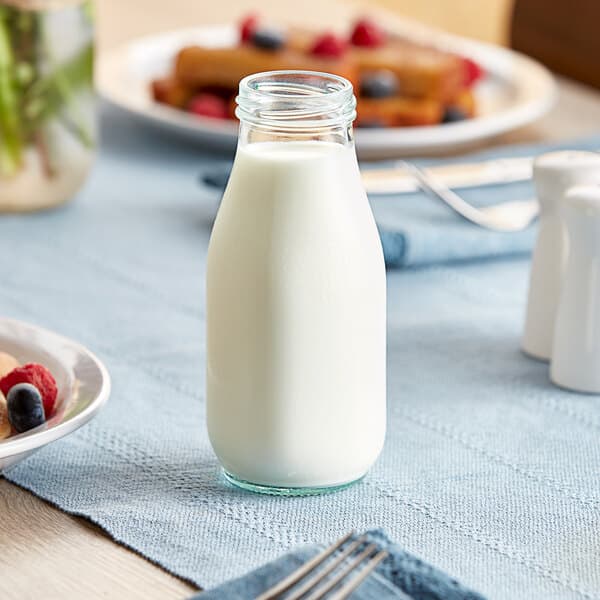An Acopa glass milk bottle on a table with a plate of fruit.