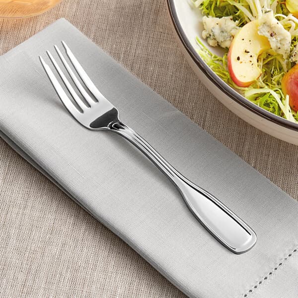 An Acopa Scottdale stainless steel salad fork on a napkin next to a bowl of salad.