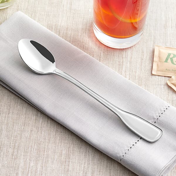 An Acopa Scottdale stainless steel iced tea spoon on a napkin next to a glass of tea.