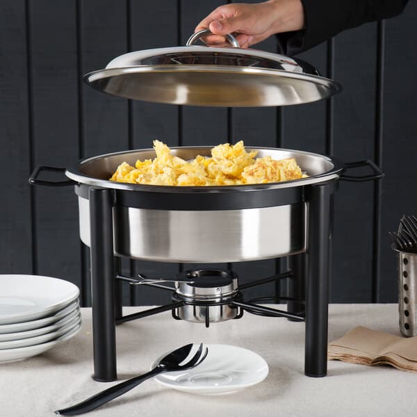 A person holding an Acopa wrought iron chafer cover over a food pot.
