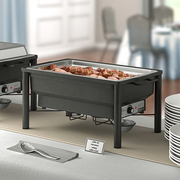 An outdoor buffet table with a rectangular chafer stand holding a large rectangular container of meat.