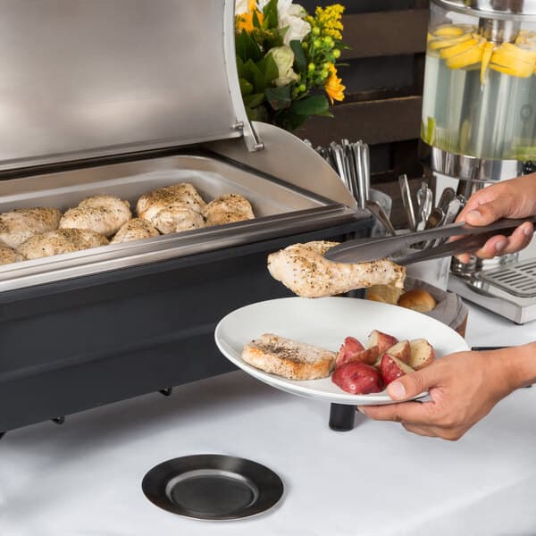 A person using an Acopa Wrought Iron Pillar Electric Chafer to serve food at an outdoor buffet.