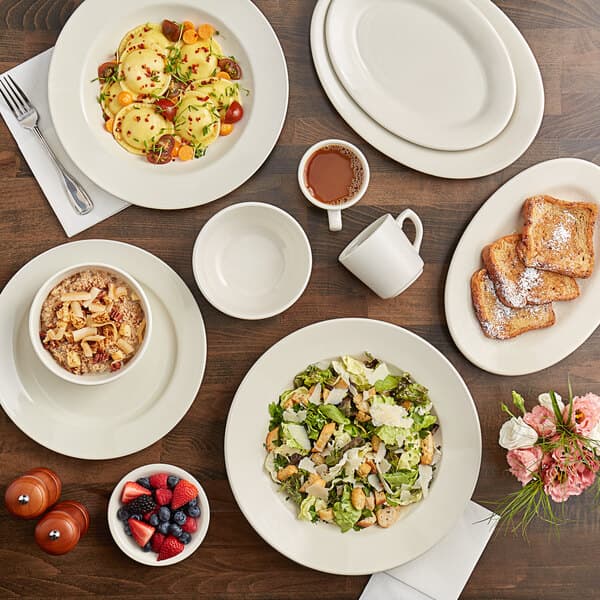 An Acopa ivory stoneware cup on a table with plates of food and drinks.