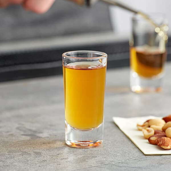 A person pouring yellow liquid into an Acopa shooter glass on a table in a cocktail bar.