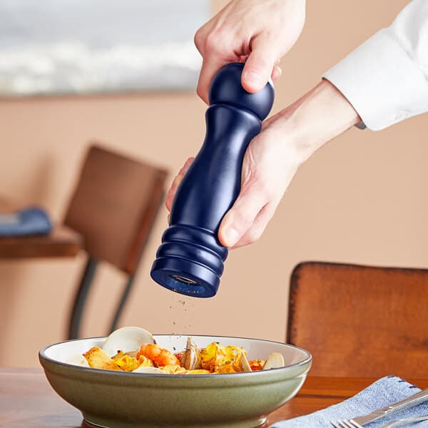 A person using an Acopa dark blue wooden pepper mill over a bowl of food.
