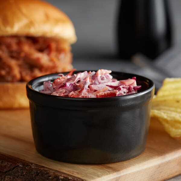 A bowl of food on a table with a sandwich and a bowl of coleslaw.