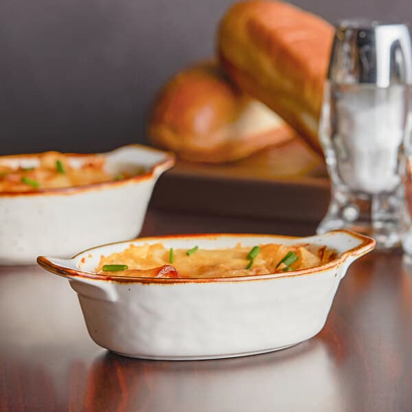 Two Acopa Keystone stoneware rarebit dishes with food on a table.