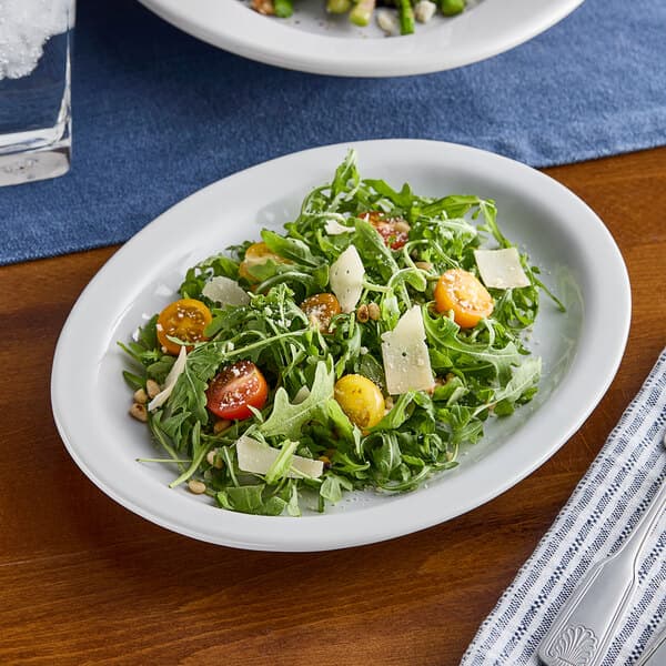 An Acopa narrow rim oval stoneware platter with a salad of arugula, tomatoes, and feta cheese.