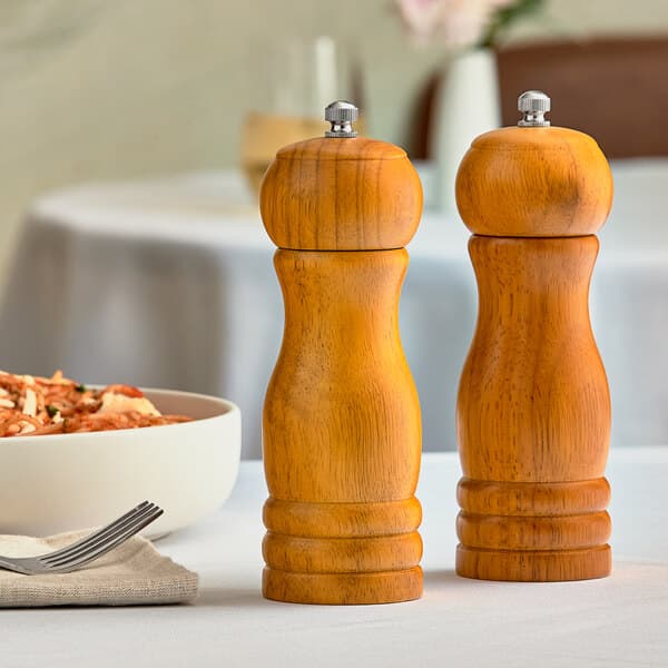 Two Acopa brown wooden salt and pepper mills on a table.