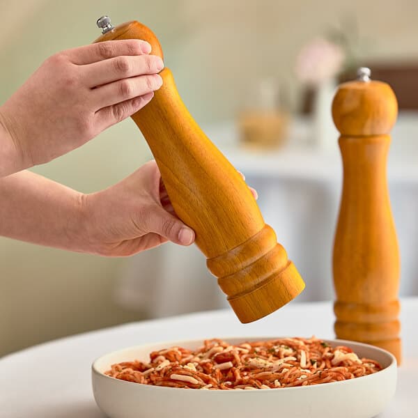A person using a wooden pepper mill to season a bowl of pasta.
