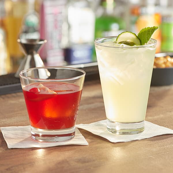 Two Acopa Fusion rocks glasses filled with drinks and ice on a table with a slice of orange.