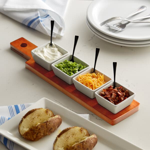 An Acopa flight paddle with square tasting bowls on a table with potatoes, white cream, and green onions.