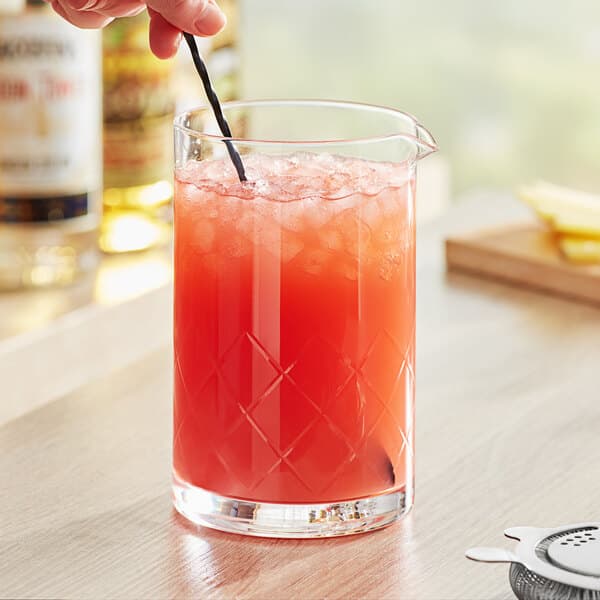 A hand using a straw to stir a red cocktail in an Acopa Diamond Cut cocktail glass.