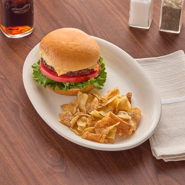 An Acopa ivory oval stoneware platter with a hamburger and chips on it.