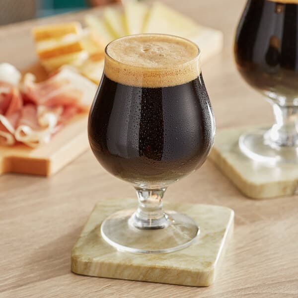 Two Acopa Select Belgian beer glasses filled with dark beer on a table in a brewery tasting room.
