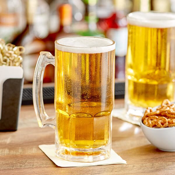 Two Acopa customizable beer mugs filled with beer on a table with a bowl of pretzels.