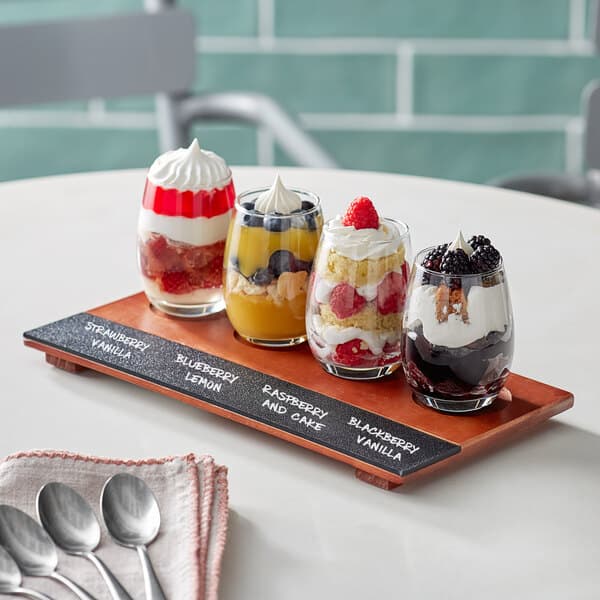 An Acopa Write-On flight tray with 6 stemless wine tasting glasses filled with desserts on a wooden table.