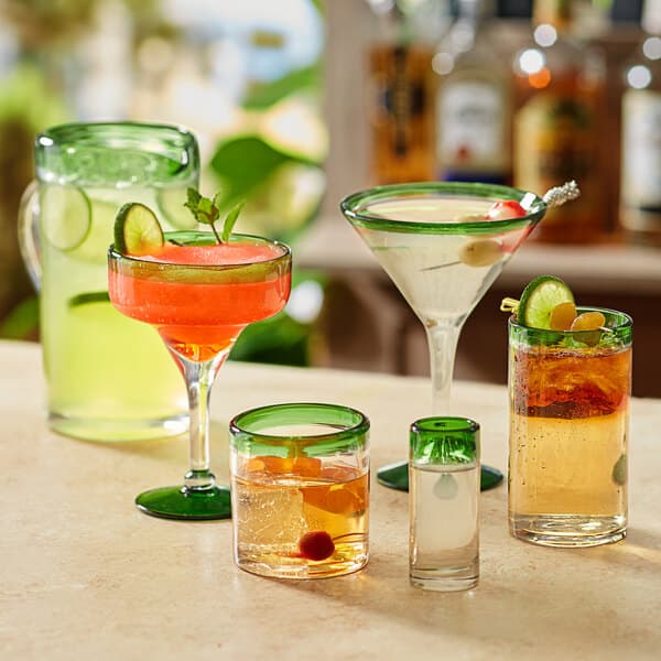 A table with a variety of drinks, including a green-rimmed martini with a cherry.