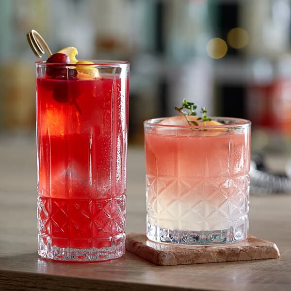 Two Acopa Evora cocktail glasses with drinks and fruit on a table.