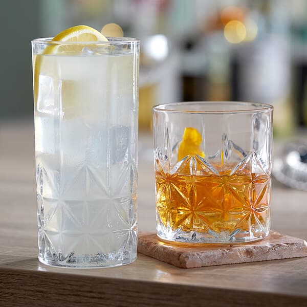 Two Acopa Gardenia rocks glasses with drinks and a lemon on a table.