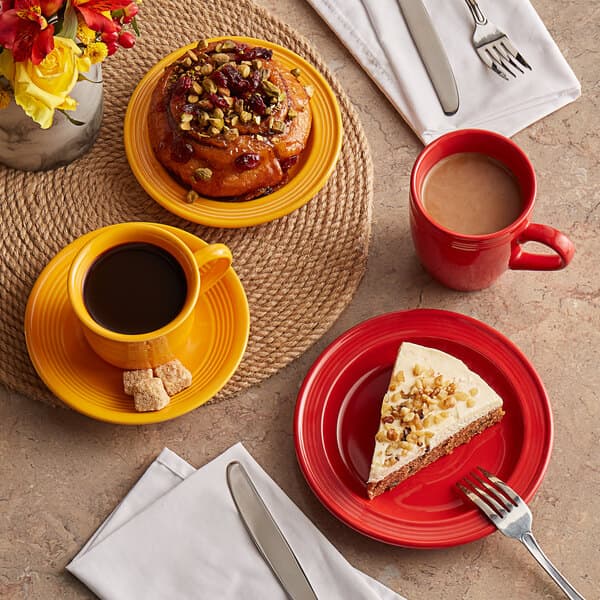 A red Acopa Capri stoneware mug filled with a liquid on a table with food and coffee.