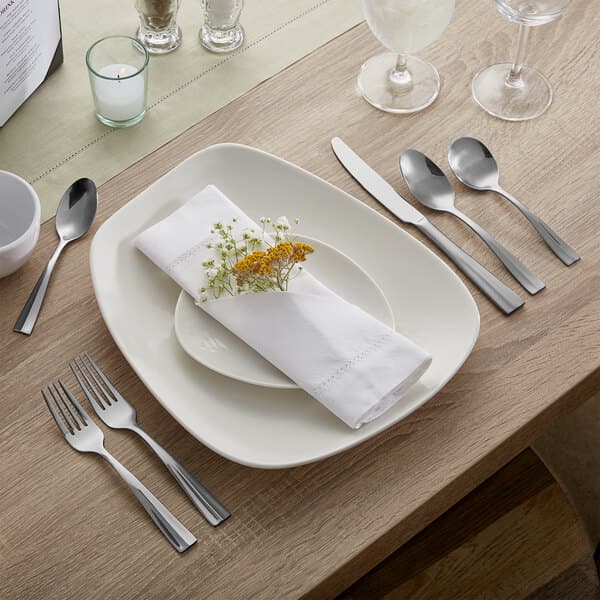 A white table with an Acopa stainless steel bouillon spoon and a plate with a flower on it.