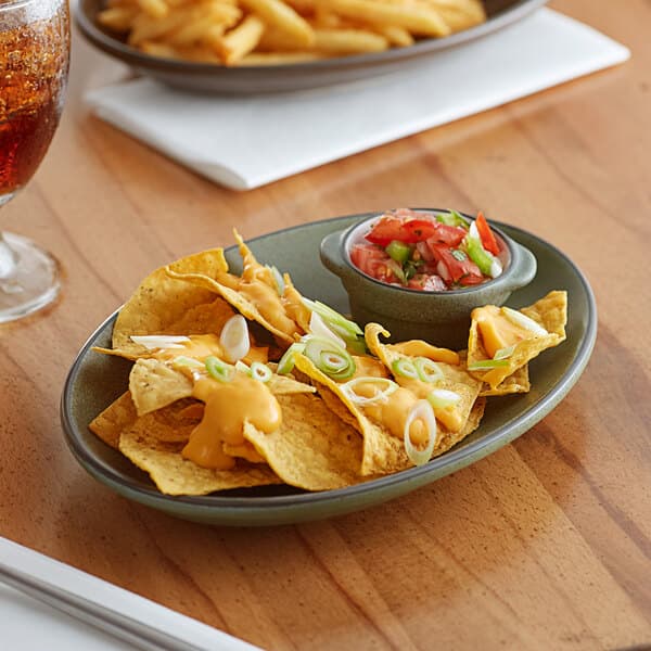 A moss green Acopa stoneware platter with nachos, salsa, and a drink on a table.