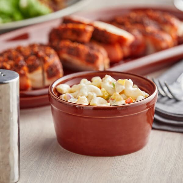 A bowl of macaroni and cheese next to a plate of meat with an Acopa Sedona Orange stoneware ramekin on the table.