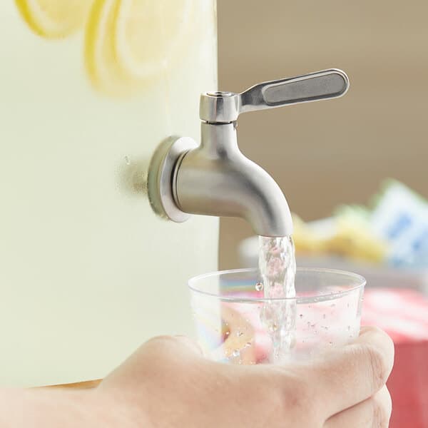A hand filling a glass with water using an Acopa stainless steel spigot.