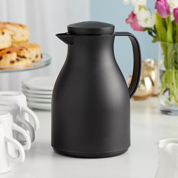 An Acopa black thermal carafe on a table with white flowers.