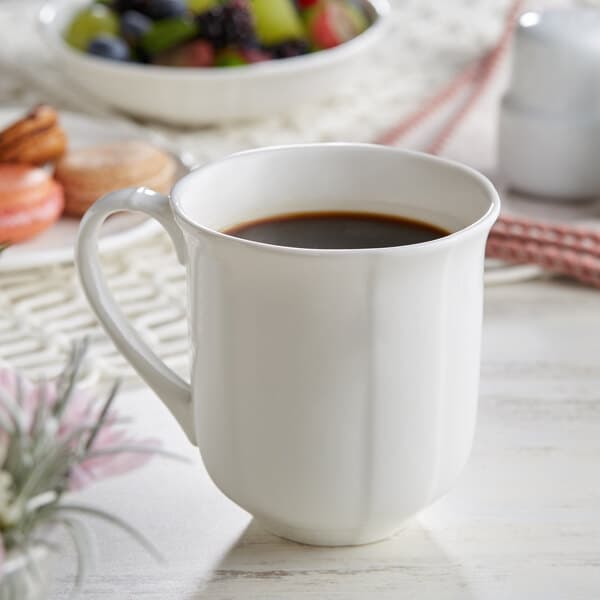 A white Acopa porcelain mug with a brown liquid and fruit on a table.