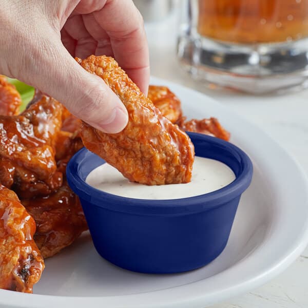 A hand dipping a piece of chicken into a blue Acopa ramekin of sauce.
