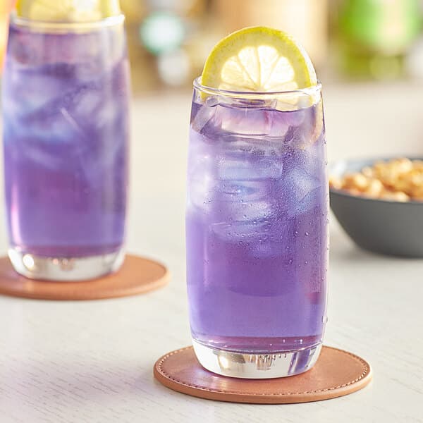 Two Acopa beverage glasses filled with purple liquid and a lemon slice on top.