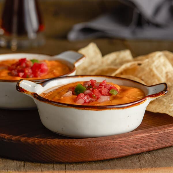 Two Acopa vanilla bean stoneware mini casserole dishes filled with food on a wooden tray.
