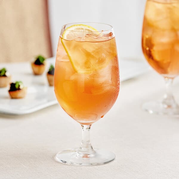 Two Acopa Covella glass goblets filled with orange liquid and a slice of lemon on a table.