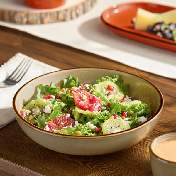 A granite gray stoneware coupe low bowl filled with a fresh salad, displayed on a wooden table.